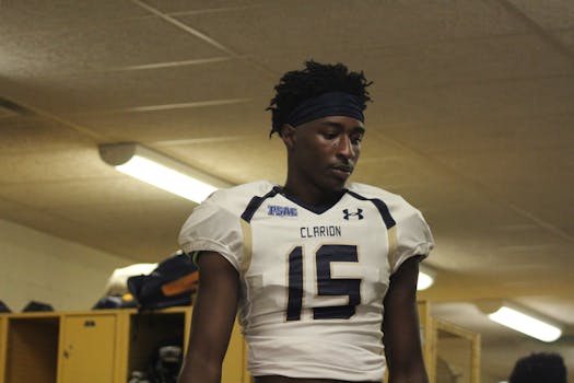 Focused football player in locker room wearing Clarion uniform, number 15, preparing for a match.