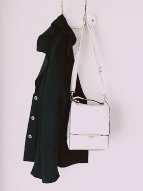 Black wool coat and white shoulder bag on a wall hook — photo by Lisa from Pexels