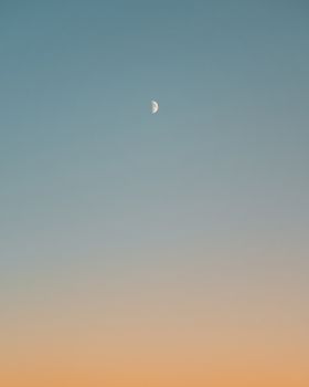 Tranquil sky showcasing a half moon during twilight with a gradient from blue to orange.