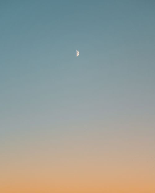 Free Tranquil sky showcasing a half moon during twilight with a gradient from blue to orange. Stock Photo