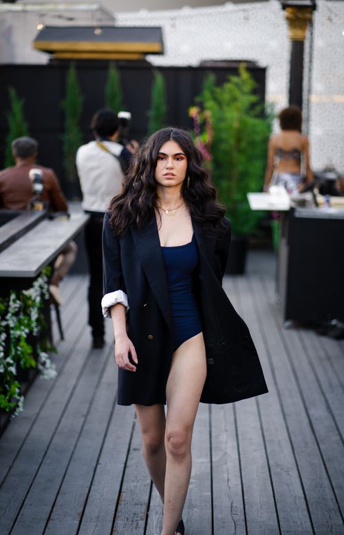 Free A woman confidently walks on an outdoor fashion runway in a chic black blazer and bodysuit. Stock Photo