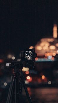 Camera on tripod capturing a cityscape at night with blurred lights in the background.