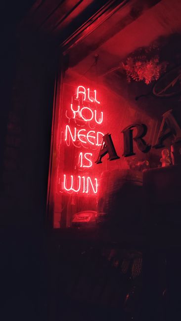 A glowing red neon sign reads 'ALL YOU NEED IS WIN' in a dark, cozy interior.