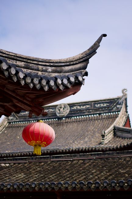 Close-up of ornate roof and red lantern at traditional Asian temple.