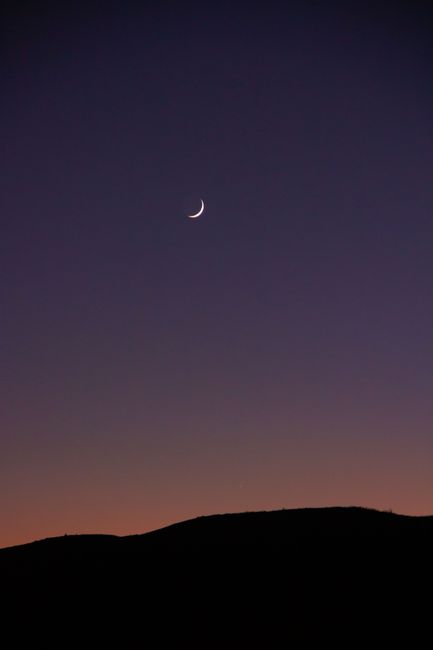 A serene crescent moon hangs over a mountain silhouette against a twilight sky, evoking tranquility.