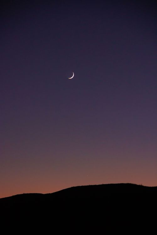 Free A serene crescent moon hangs over a mountain silhouette against a twilight sky, evoking tranquility. Stock Photo
