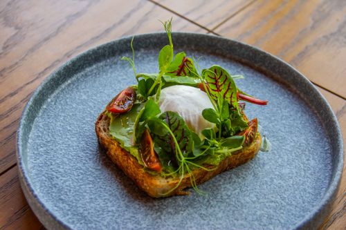 Free Delicious avocado toast topped with fresh greens and a poached egg, served on a rustic ceramic plate. Stock Photo