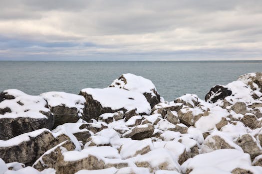 Scenic view of snow-covered rocks by Lake Ontario with a cloudy winter sky.