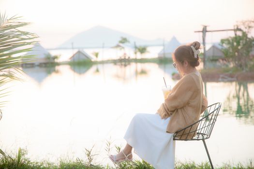A woman enjoys a tranquil moment by the lakeside, sipping a drink.