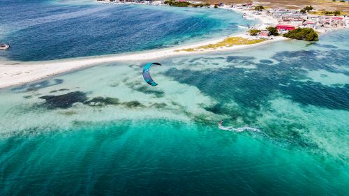Free Stunning aerial shot of a kitesurfer navigating a turquoise sea along a sandy tropical coastline. Stock Photo