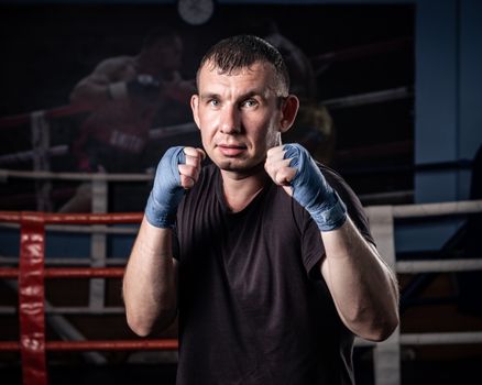 A determined boxer with blue hand wraps posing in a gym boxing ring.