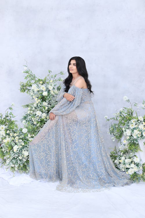 A Woman in Beautiful Blue Gown Sitting Near White Flowers while Looking Afar