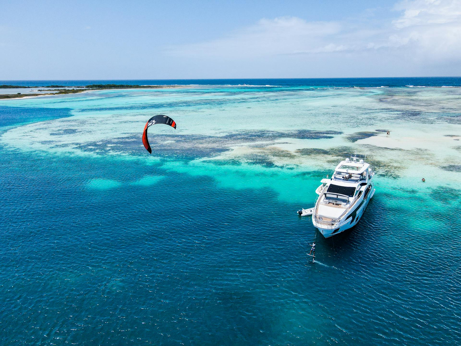 Drone shot of a luxurious yacht with a kite surfer on the turquoise sea, showcasing coastal beauty.