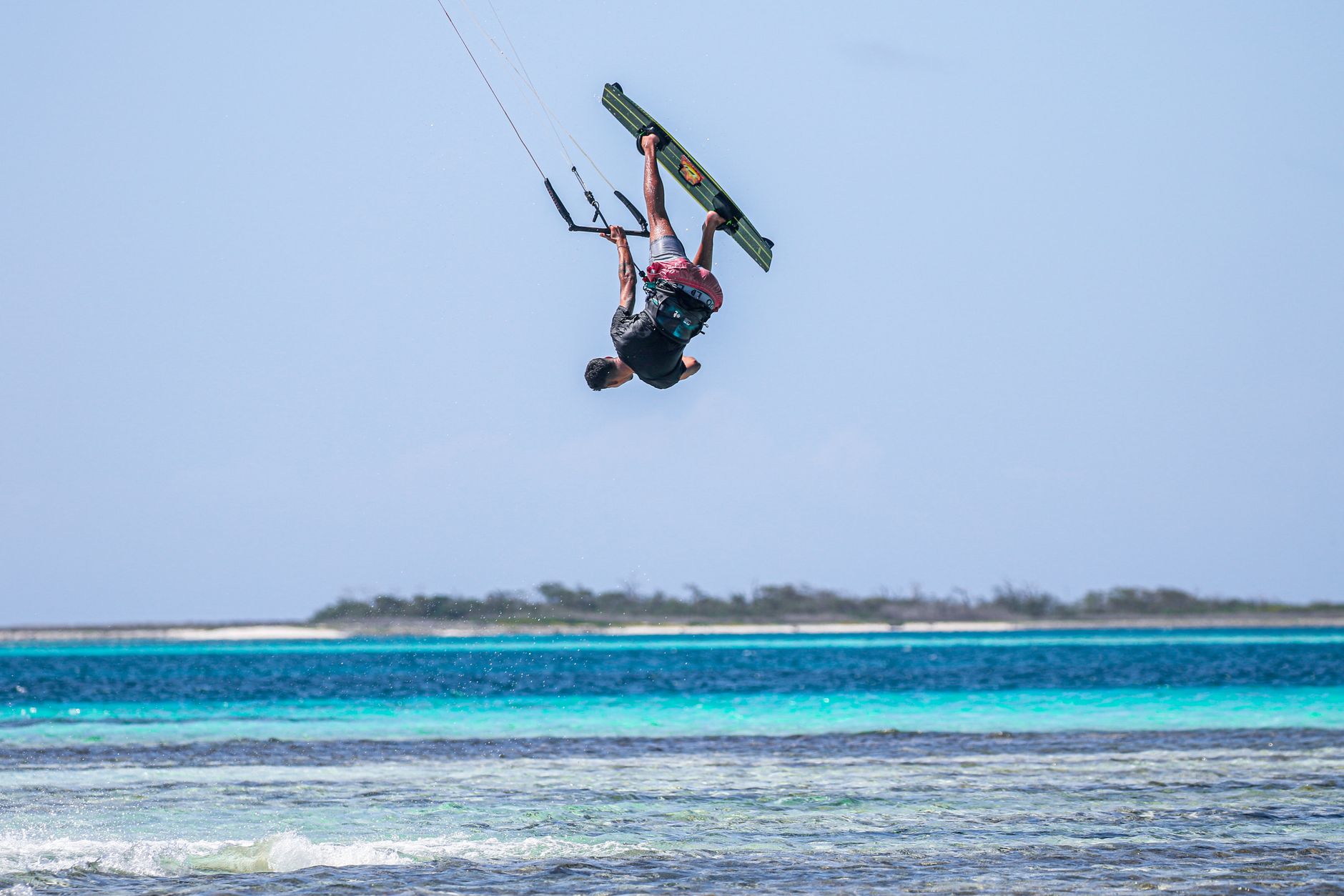 A thrilling kitesurfing trick captured mid-air over a beautiful ocean setting.