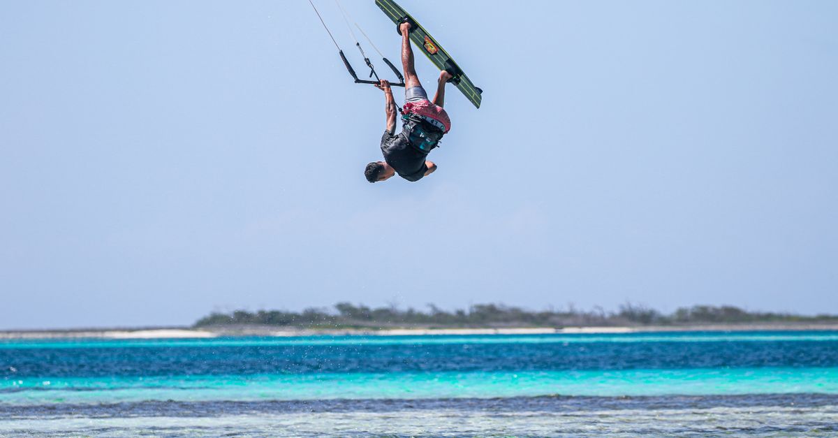 A thrilling kitesurfing trick captured mid-air over a beautiful ocean setting.
