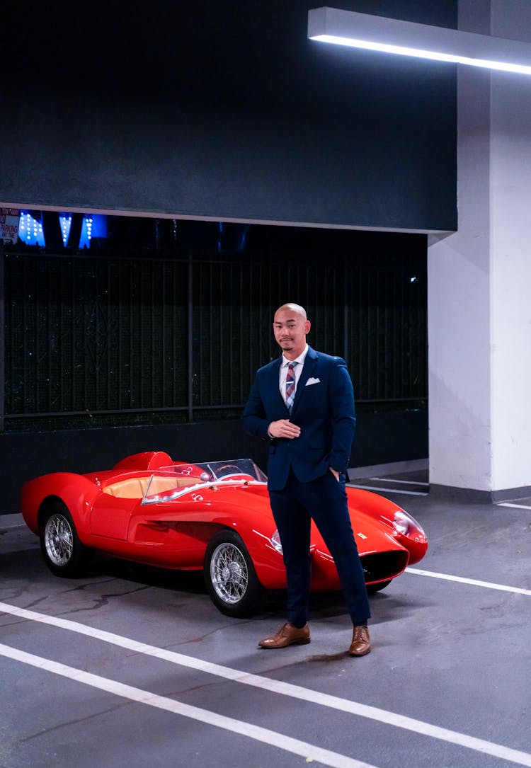 Photo Of A Man In A Suit Standing In Front Of A Red Retro Racing Car