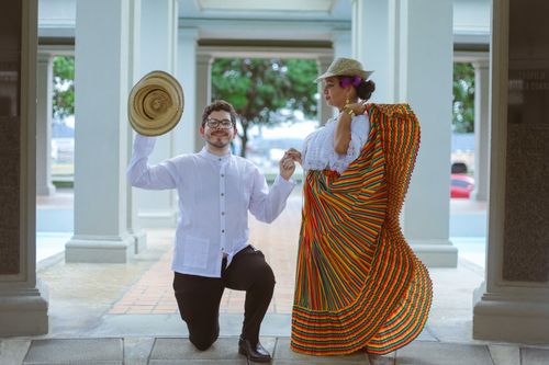 Free A man and woman in traditional Latin American attire pose outdoors. The man kneels with a straw hat. Stock Photo