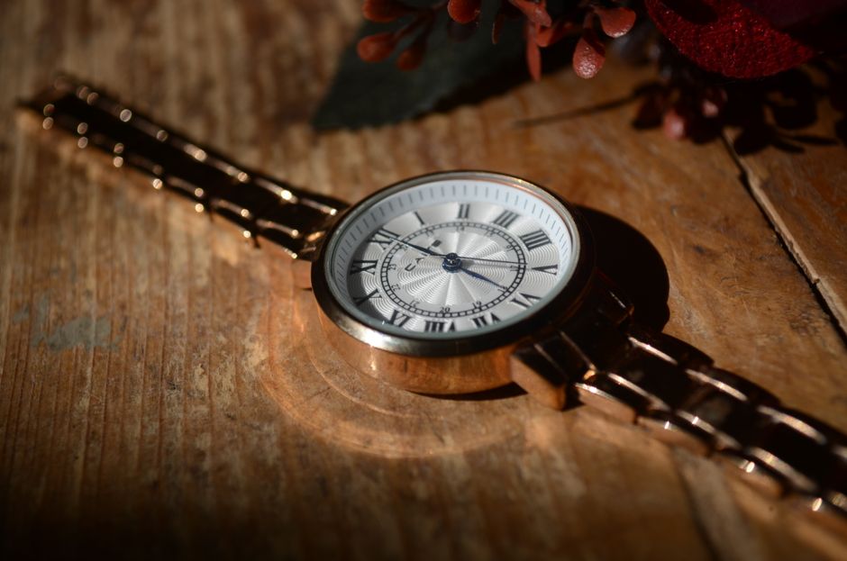 Close-up of a vintage wristwatch with a metal strap and Roman numerals on a rustic wooden surface.