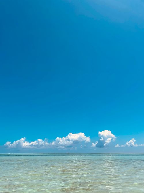 Free A serene view of tropical turquoise waters under a bright blue sky with fluffy clouds. Stock Photo