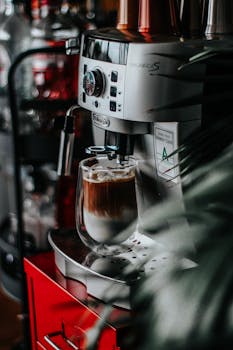 Vertical close-up of a stainless steel espresso machine brewing a rich coffee in a cozy indoor setting.