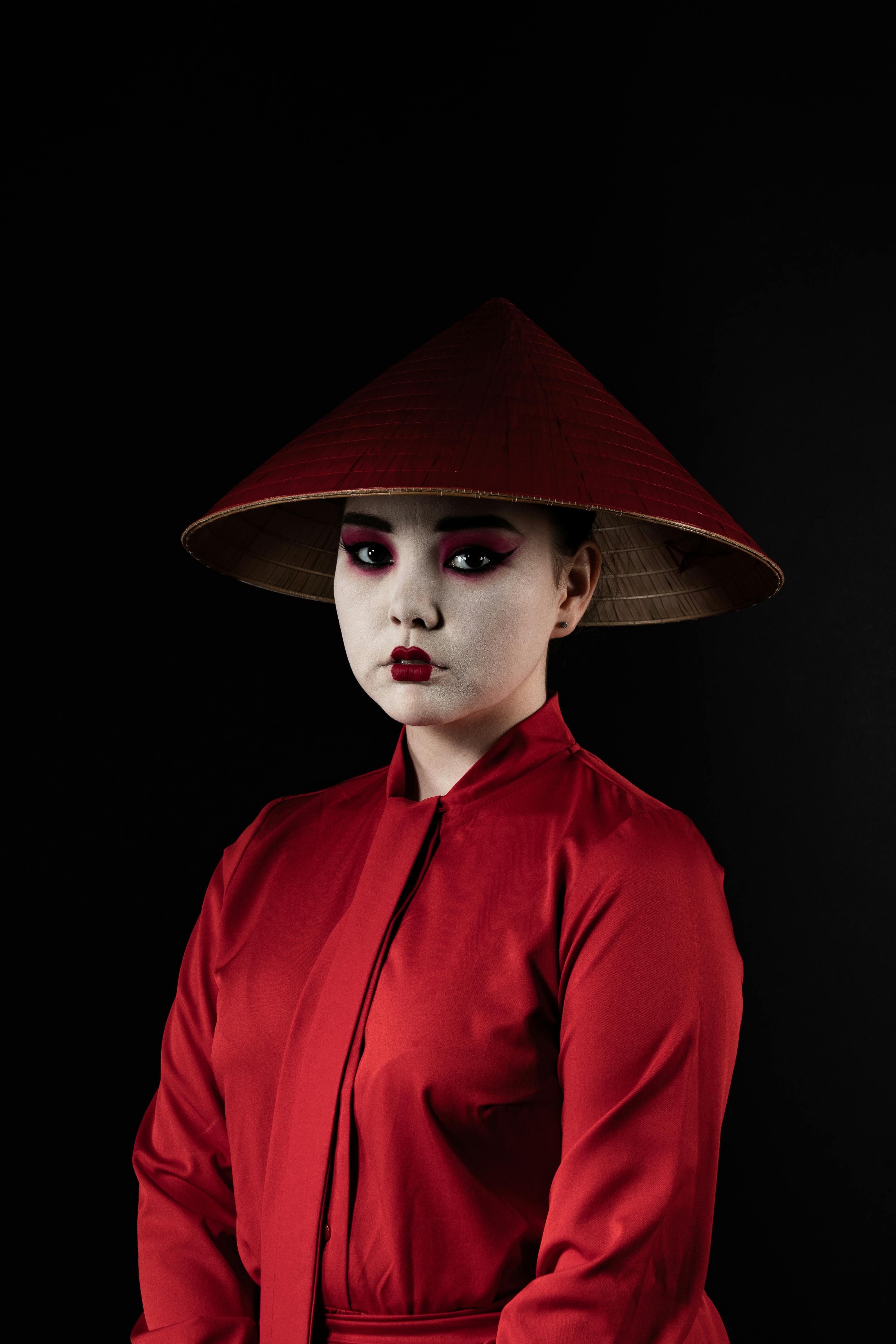 Studio shot of woman in red traditional clothing with conical hat on black background.