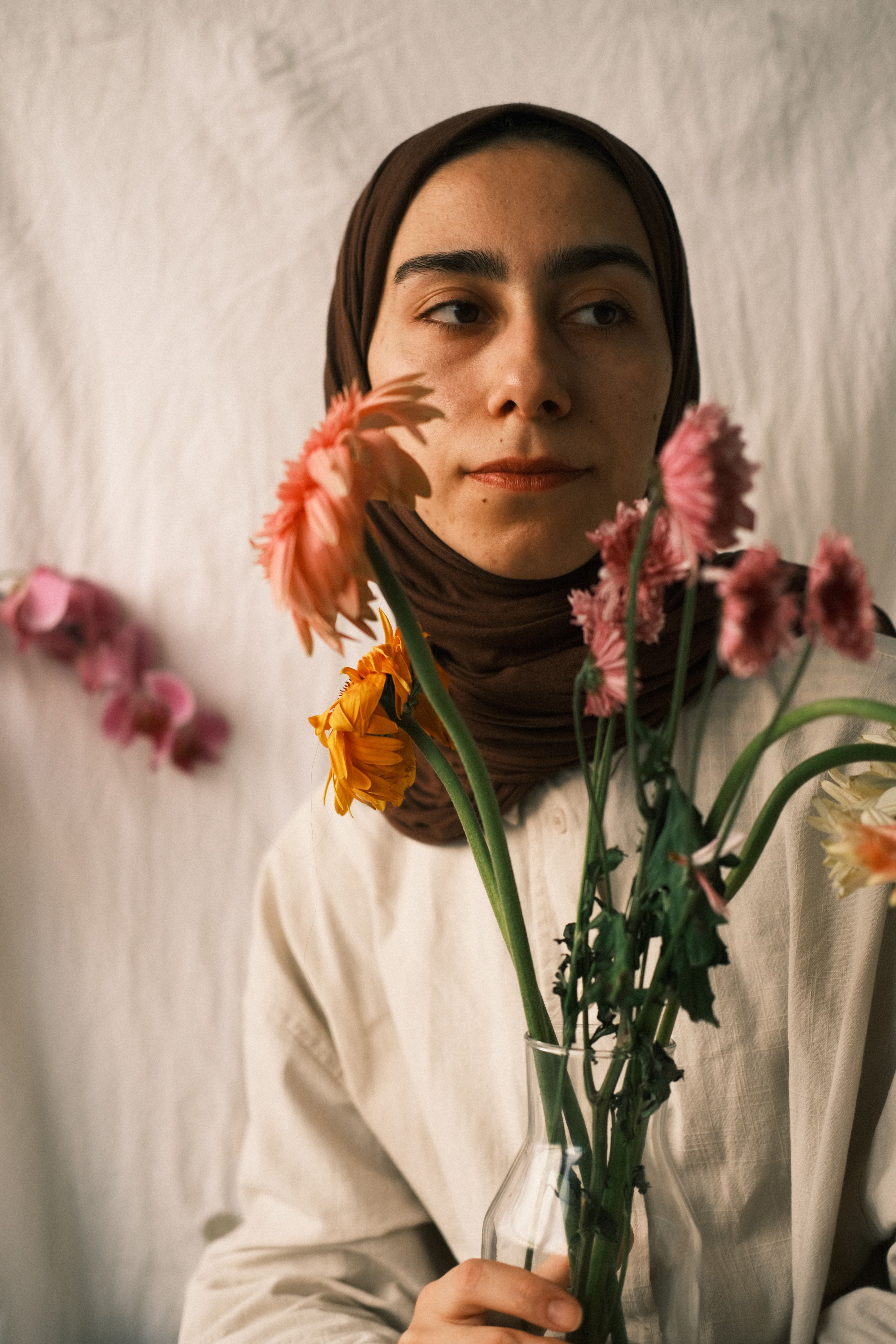 Portrait of a young woman in a hijab holding colorful flowers indoors with soft lighting.