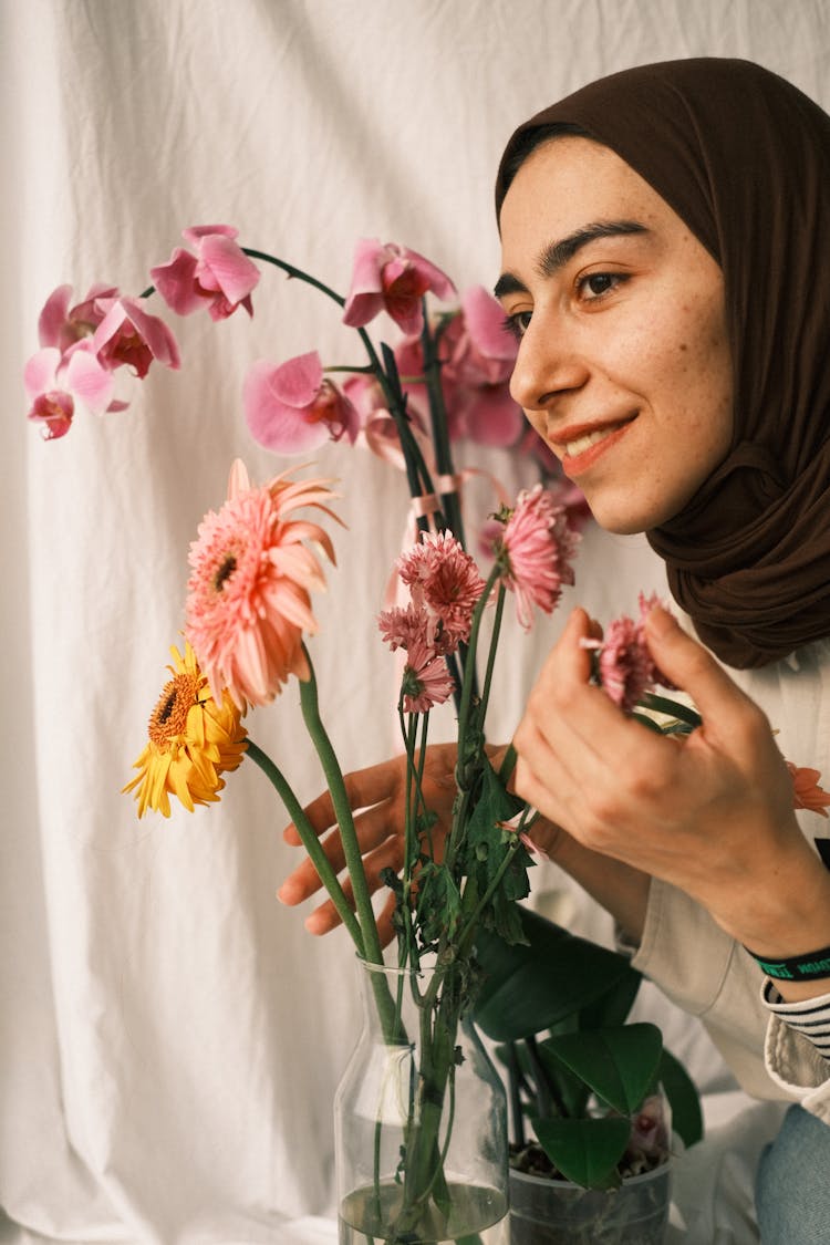 Woman Wearing A Hijab Smiling Beside Pink Flowers In A Vase