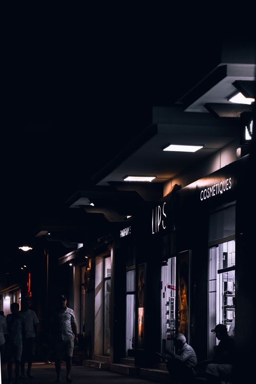 Free A bustling urban street at night featuring illuminated shops and silhouettes of people, creating a vibrant cityscape. Stock Photo