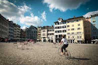 一名骑自行车的人穿过充满活力的城市广场，在明亮的天空下，周围环绕着色彩缤纷的建筑