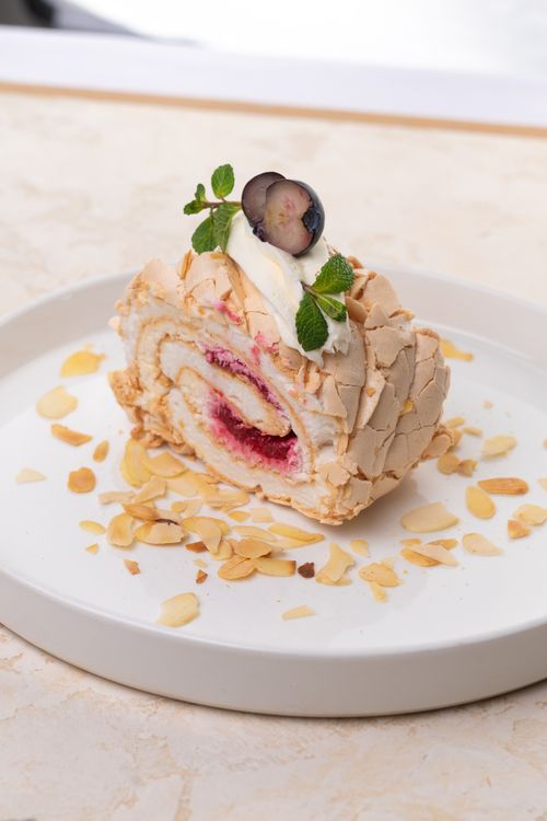 Free Mouth-watering meringue roulade topped with berries and cream, set on a white plate. Stock Photo