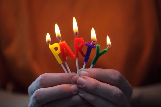 Bright party candles spelling 'PARTY' held in hands, symbolizing celebration.