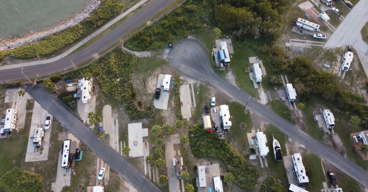 Aerial shot of a coastal RV park with campers and road, surrounded by greenery.