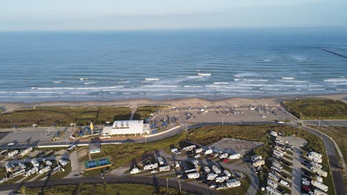 Aerial Footage of Rows of Campers Parked by a Seaside, and Waves in the Sea