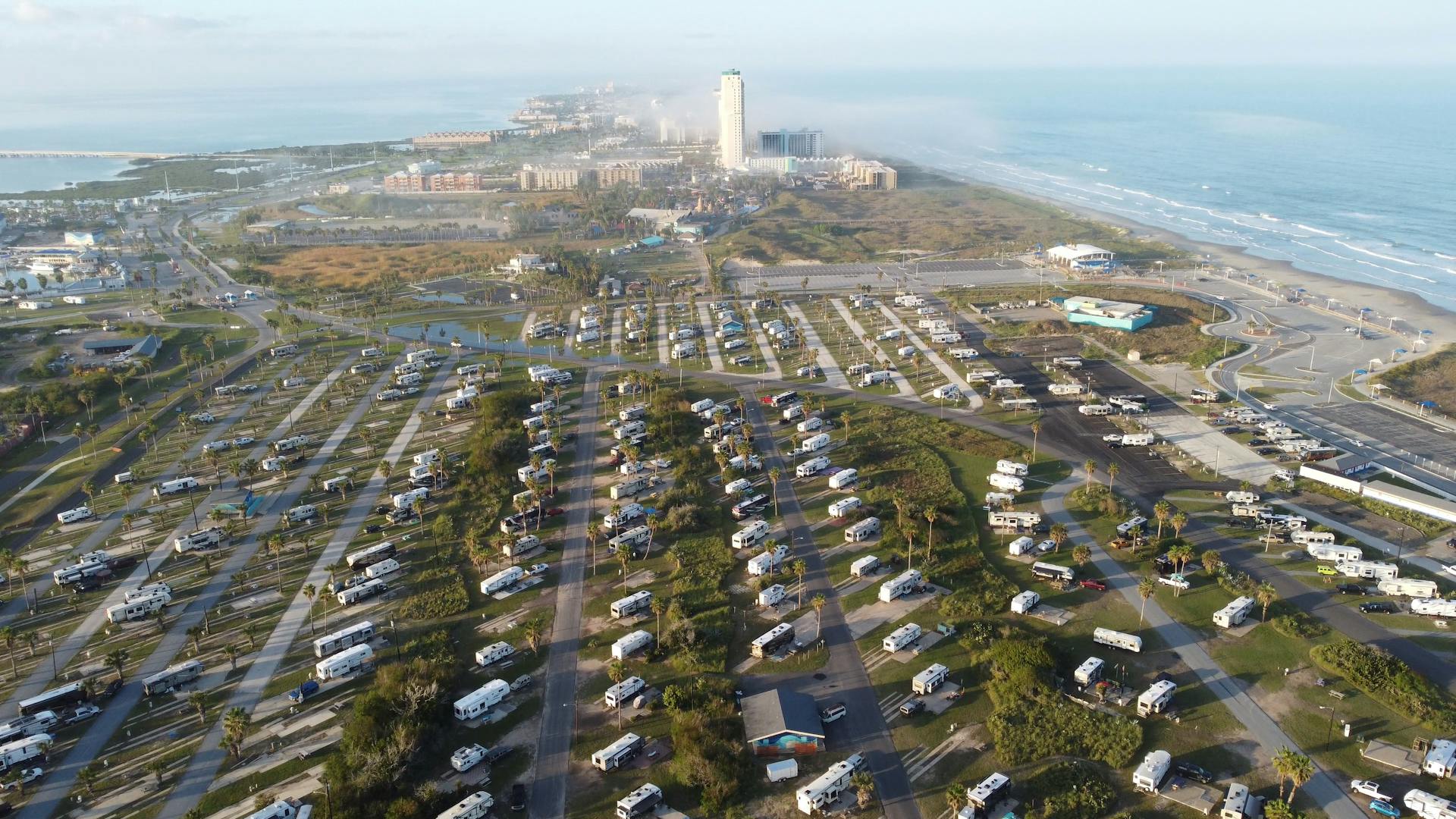 Aerial view of a coastal RV park near the ocean, showcasing numerous caravans and nearby resort buildings.