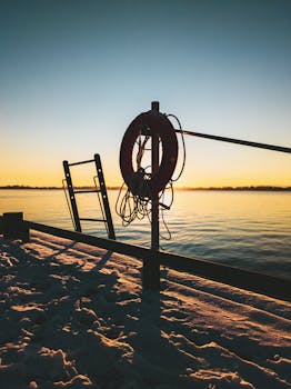 Serene winter sunrise over snow-covered lake promenade with lifebuoy and ladder.
