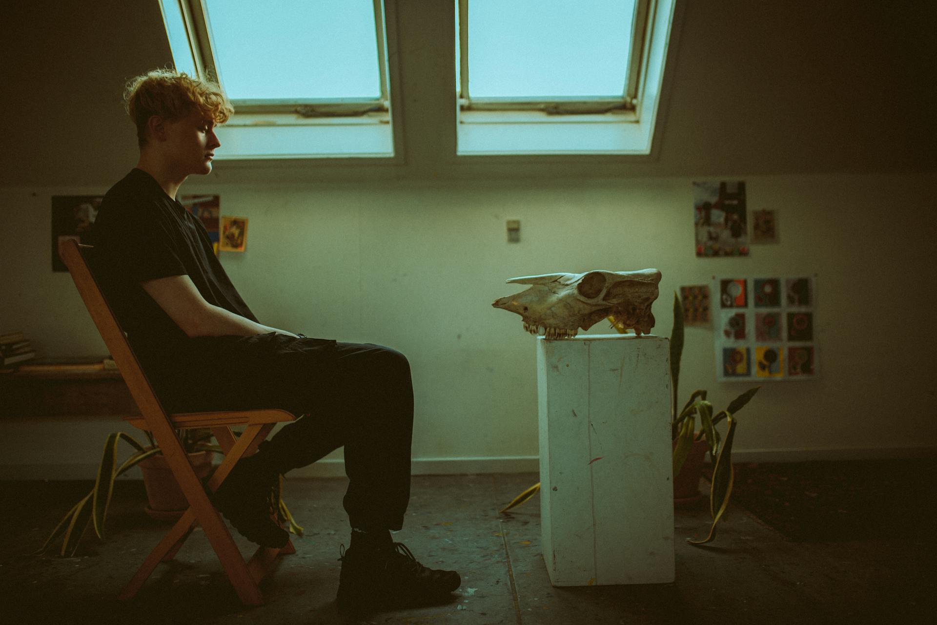 Man Sitting on a Chair in front of an Animal Skull