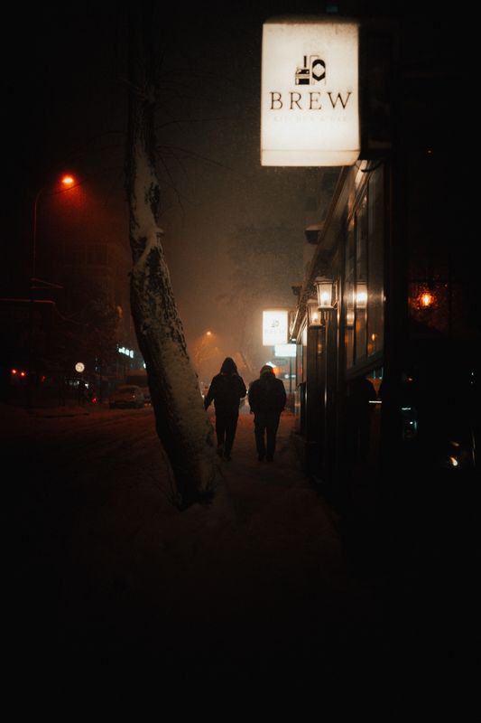 Gece loş ve karlı bir sokakta yürüyen iki kişi