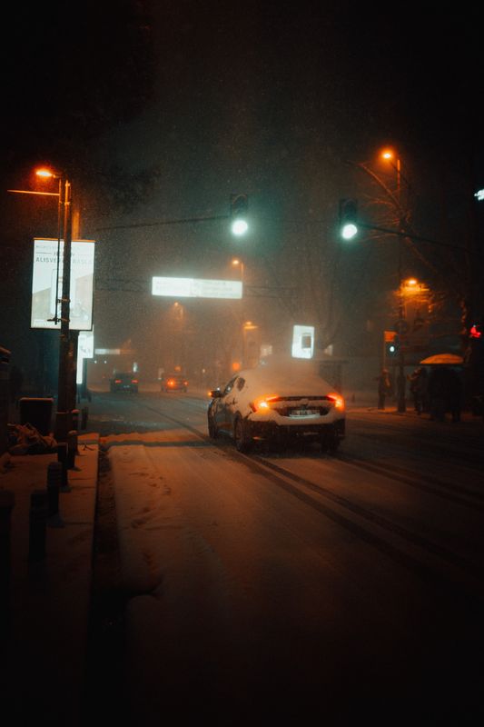 Gece sıcak lambalarla aydınlanan karlı bir sokakta bir araba