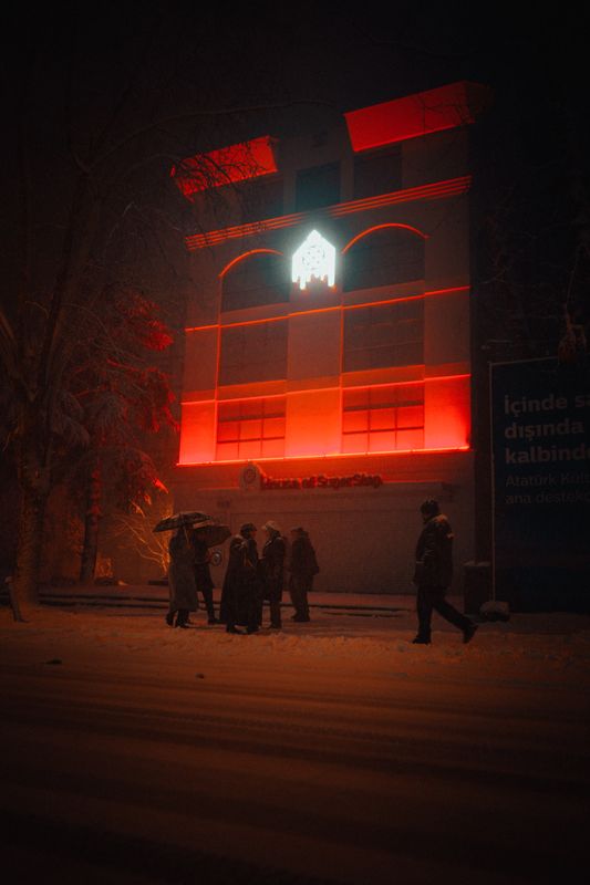 Gece kar yağarken kırmızı ışıklı bir bina ve insanlar