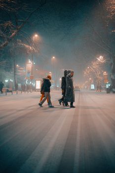 Group of people crossing a snowy street at night, illuminated by city lights.