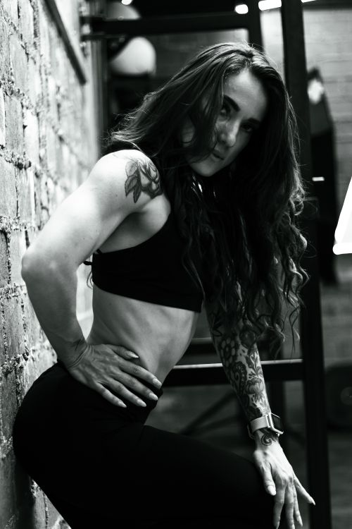 Free Elegant black and white portrait of a woman in a sports bra leaning against a brick wall. Stock Photo