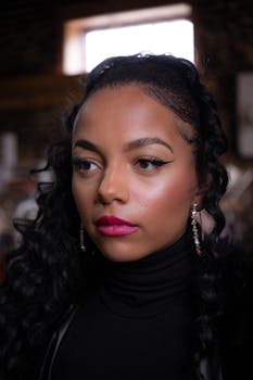 Striking portrait of a woman with bold makeup, stylish earrings, and black turtleneck indoors.