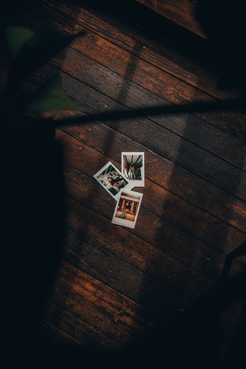 Free Three vintage Polaroid photos placed on a dark, rustic wooden floor with an artistic shadow overlay. Stock Photo