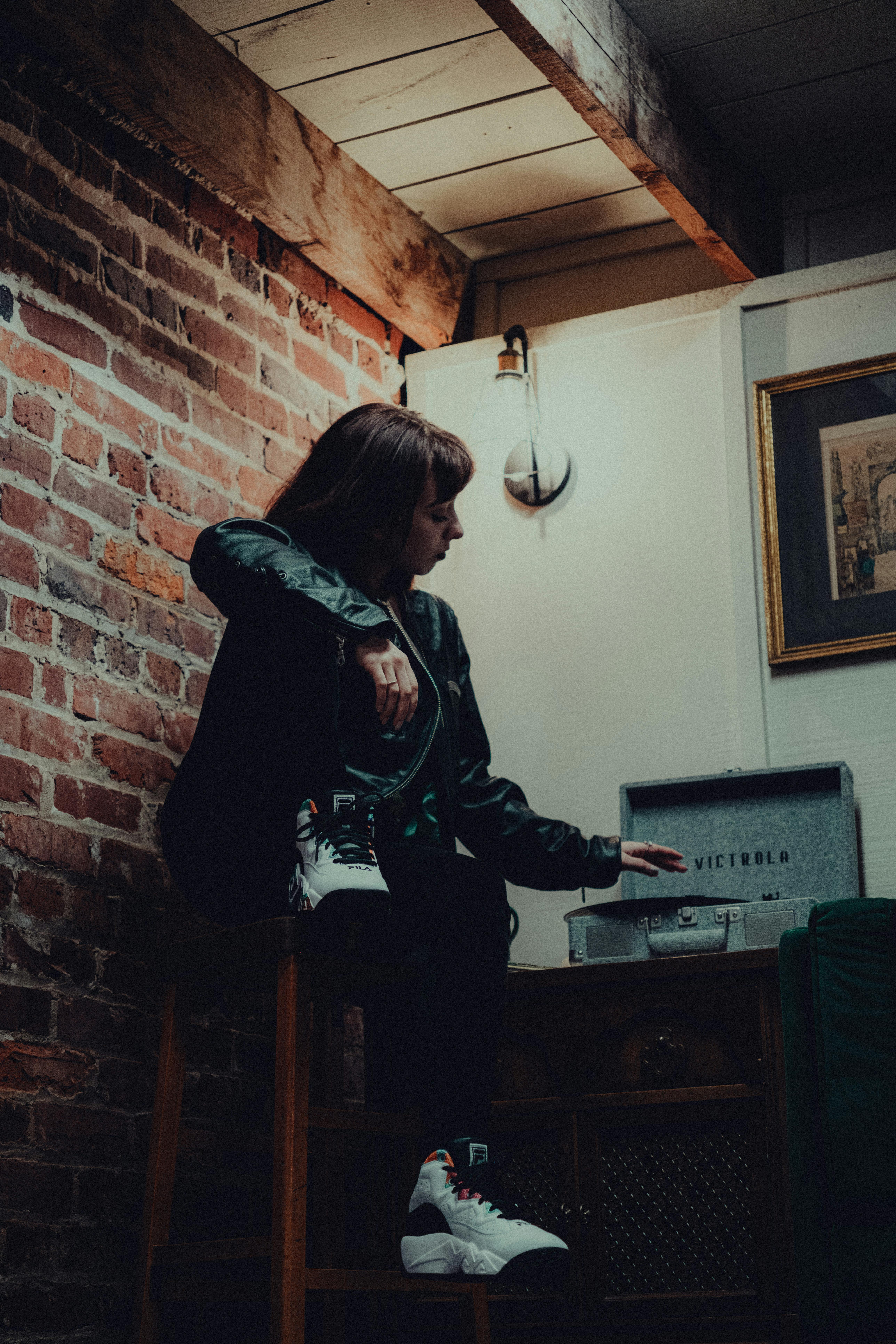 a woman sitting on a stool in front of a brick wall