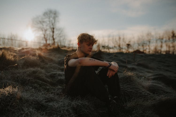 Blond Man Sitting Alone On Grass 