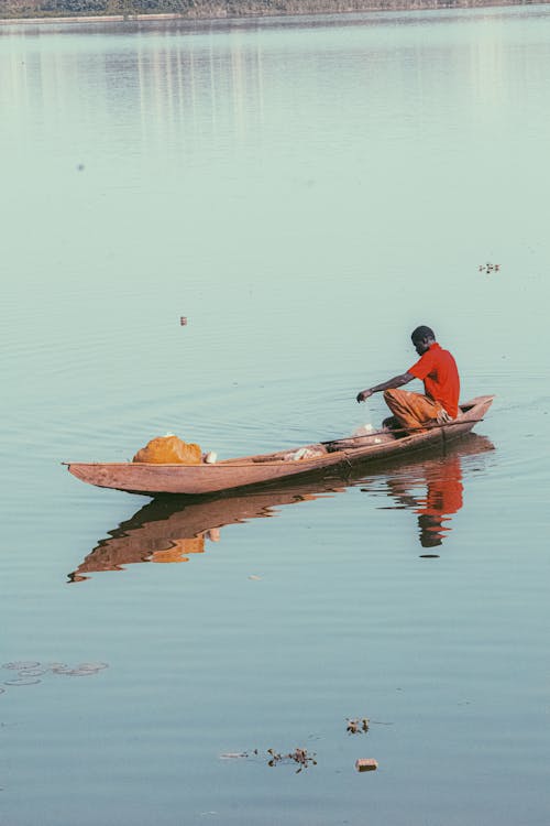 A Person Wearing Orange Shirt Riding a Boat in a Body of Water