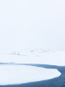 Peaceful winter scene with snow overlay and icy river under a cloudy sky.