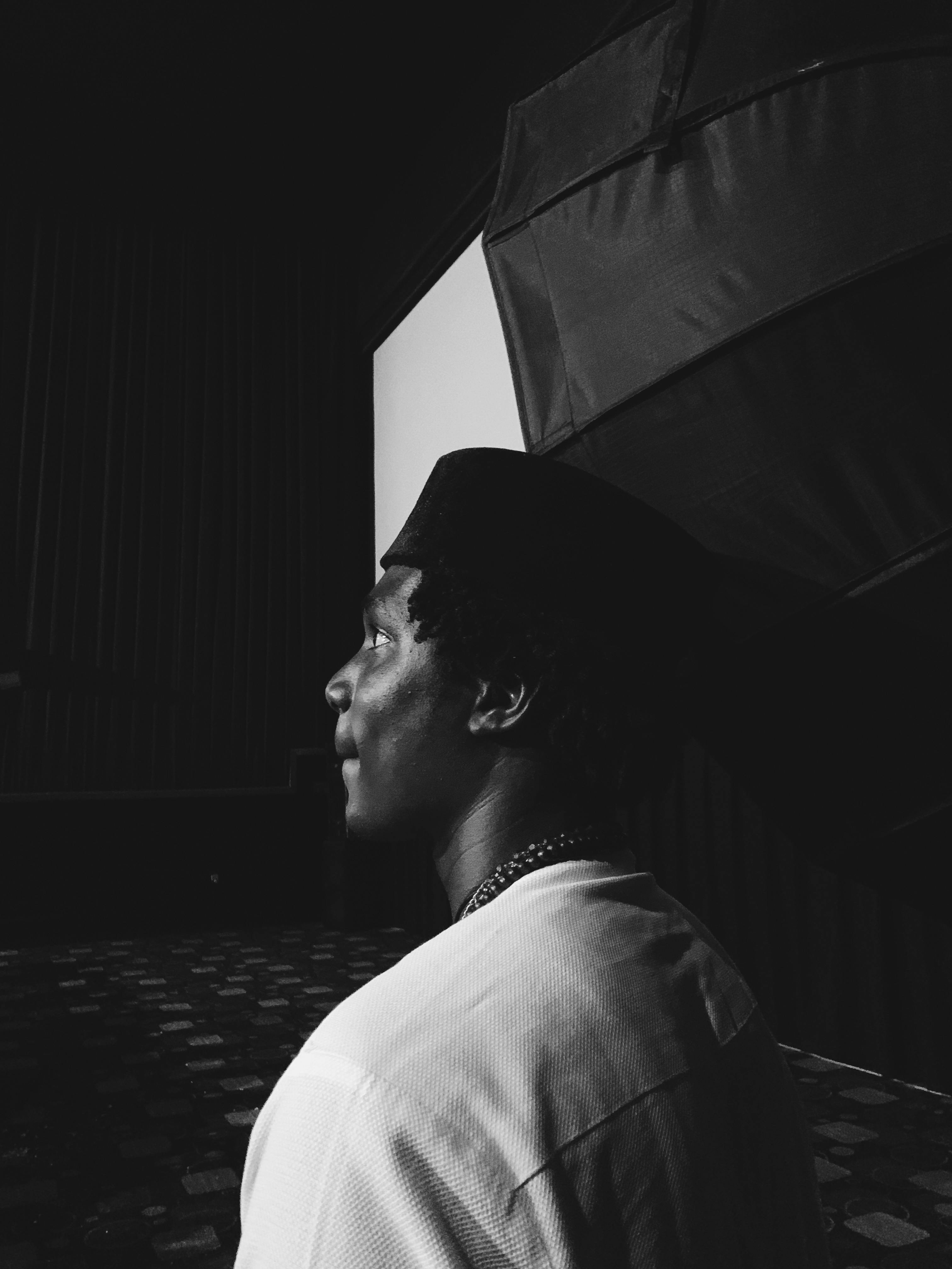 Black and white side profile of a man wearing a hat in moody lighting.