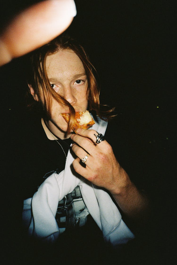 Photo With A Flash Of A Young Man Standing Outside In The Dark And Eating 