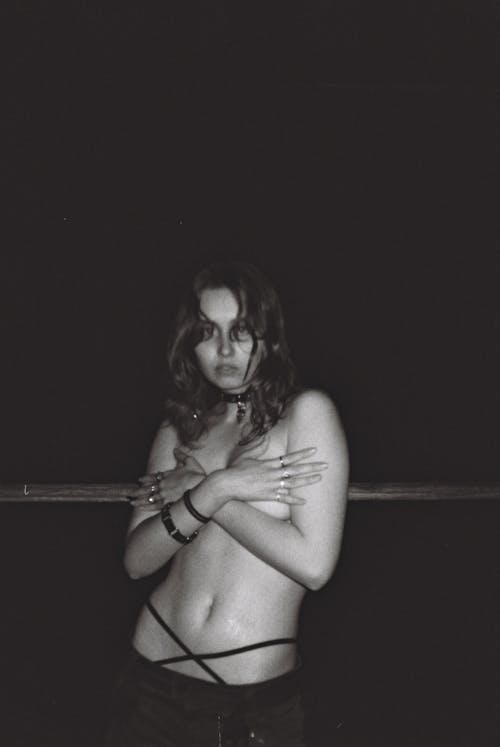 Black and White Photo of a Shirtless Young Woman Covering Her Breasts